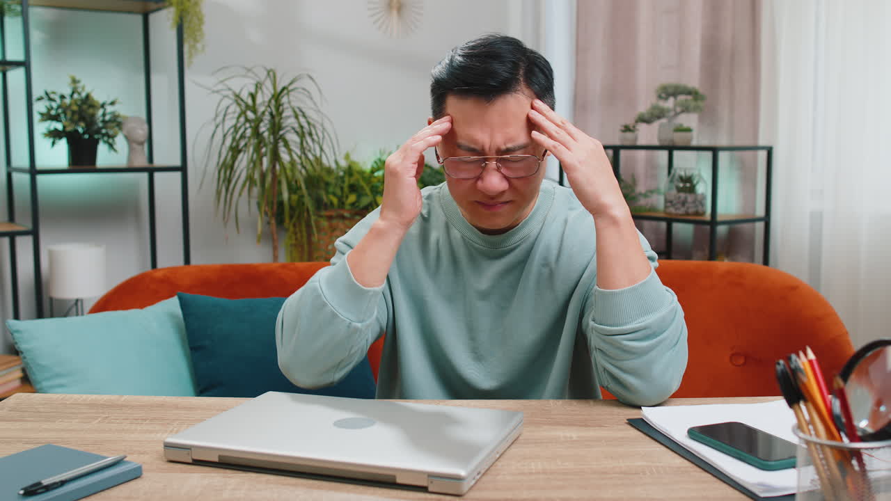 Tired asian man freelancer use laptop suffering from headache problem tension and migraine stress