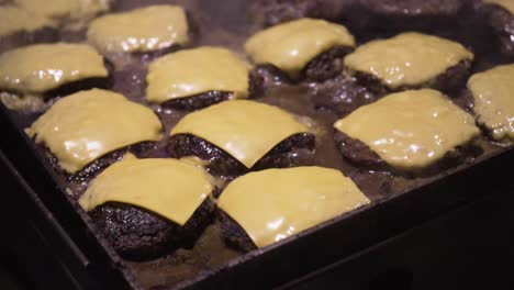 cheeseburgers cooking on a flat top griddle with steam