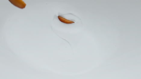 ripe apricot pieces falling on creamy yogurt in super slow motion close up.