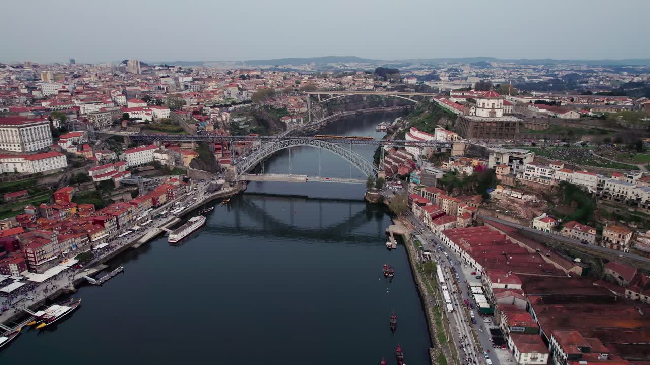 Porto high and wide cityscape featuring the iconic Dom Luis I bridge spanning the Douro river, with vibrant historic buildings lining the banks and traditional rabelo boats sailing, drone orbiting
