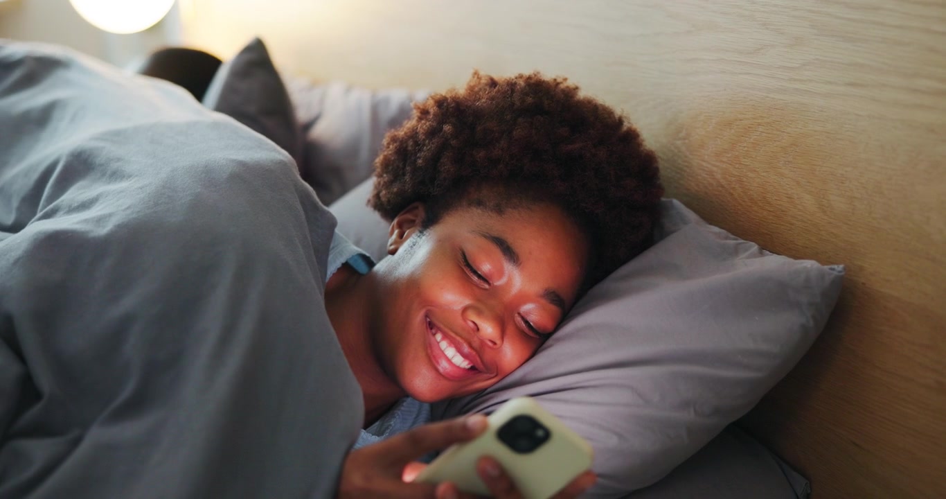Young Woman Using Smartphone in Bed While Partner Sleeps