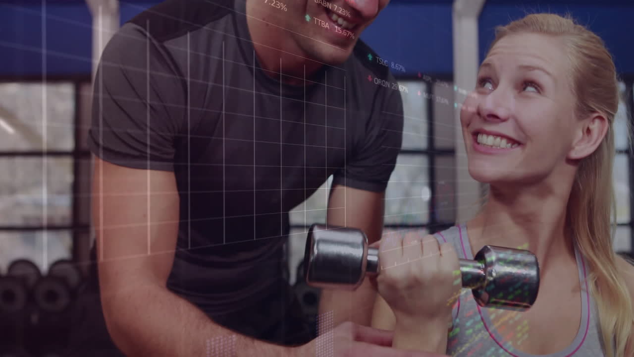 fitness client lifting dumbbell while trainer assisting in commercial gym, showing animated charts