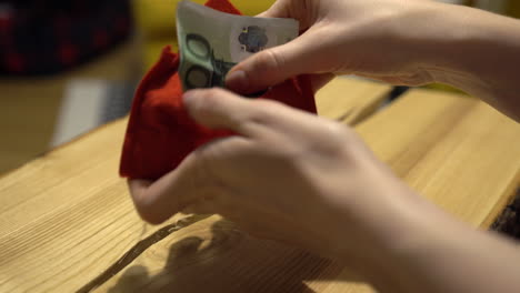 woman hands packing one hundred euro banknote into a red christmas decorated envelope