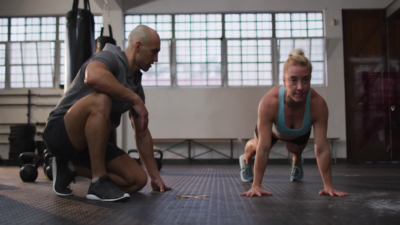 체육관 에서 남성 트레이너 와 함께 푸시 업 운동 을 하는 튼튼 한 백인 여성