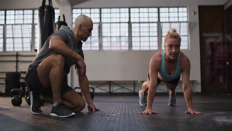 Fit-caucasian-woman-performing-push-up-exercise-with-male-trainer-at-the-gym