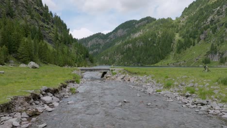 plano amplio que muestra a un ciclista de montaña montando en un pequeño puente sobre un arroyo rocoso en las montañas