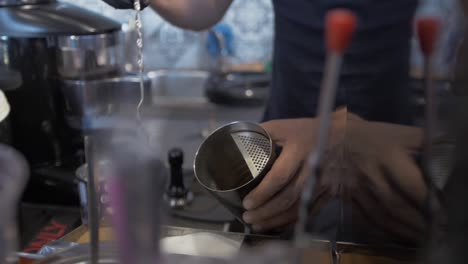barista coloca una cucharada de azúcar en una taza de acero inoxidable y hace un frappé