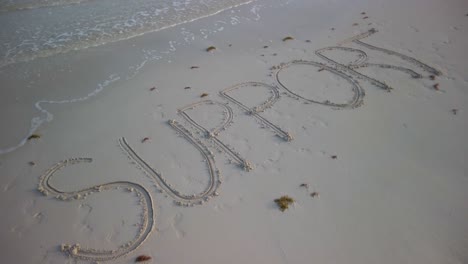 Drehende-Aufnahme-Von-Unterstützung,-Die-An-Einem-Strand-In-Den-Sand-Geschrieben-Wurde