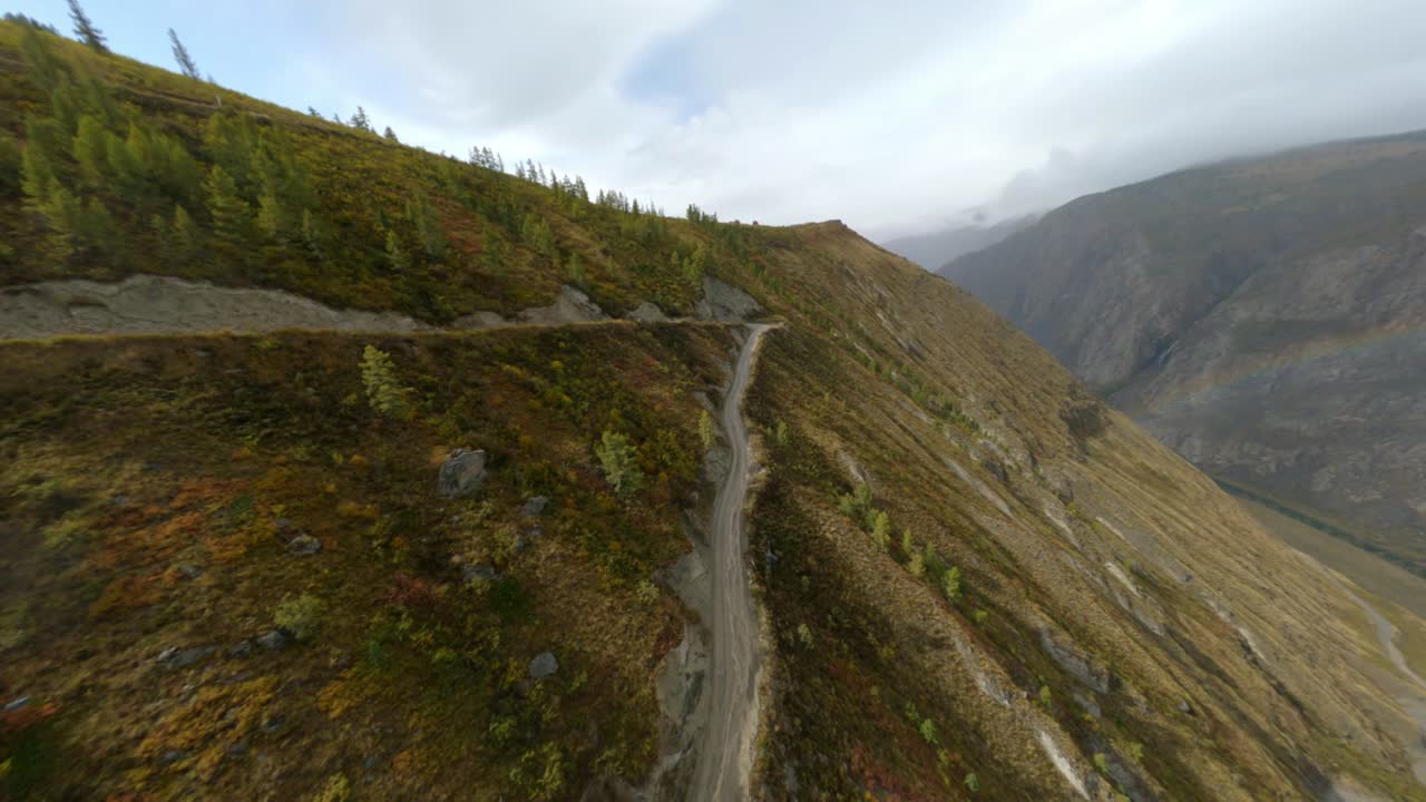 Black automobile riding on dangerous path with rainbow over valley scenery