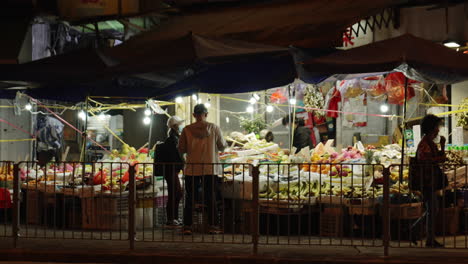 static shot of locals shopping in a food market at night in an asian town