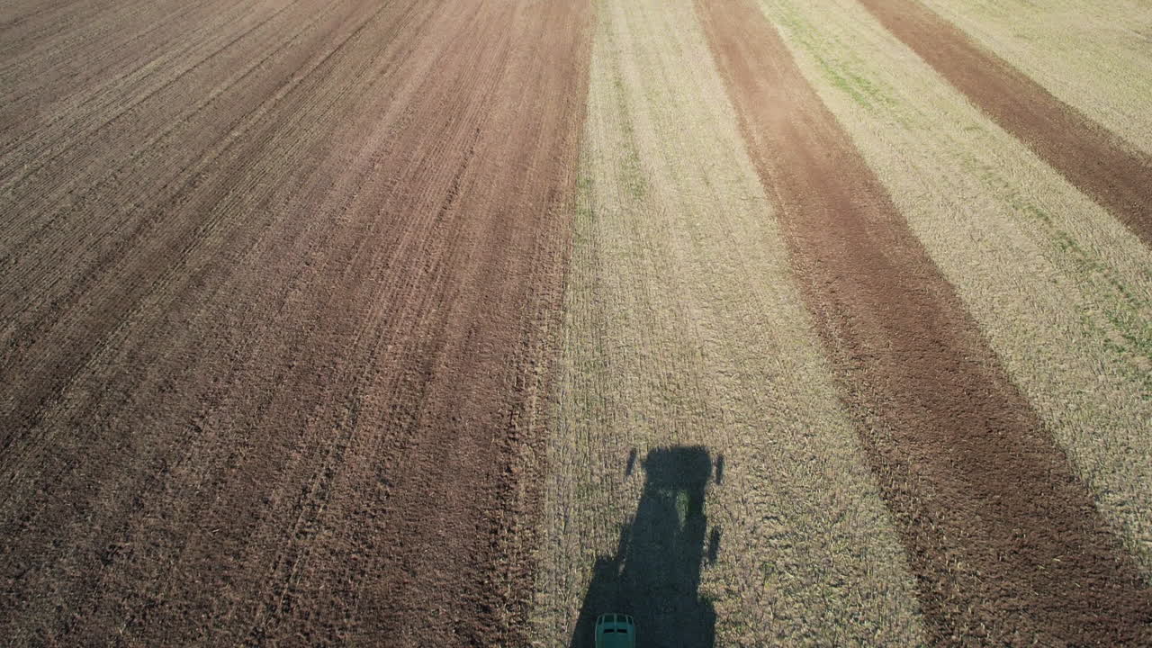 Veduta aerea a volo d'uccello di un trattore che ara la terra in un grande campo agricolo in una mattinata di sole, ripresa con drone