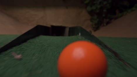 an orange mini golf ball barely misses going into the last section of the course