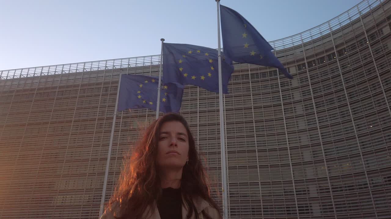 Slow motion shot of woman standing outside European Commission Berlaymont with EU flags waving in Brussels
