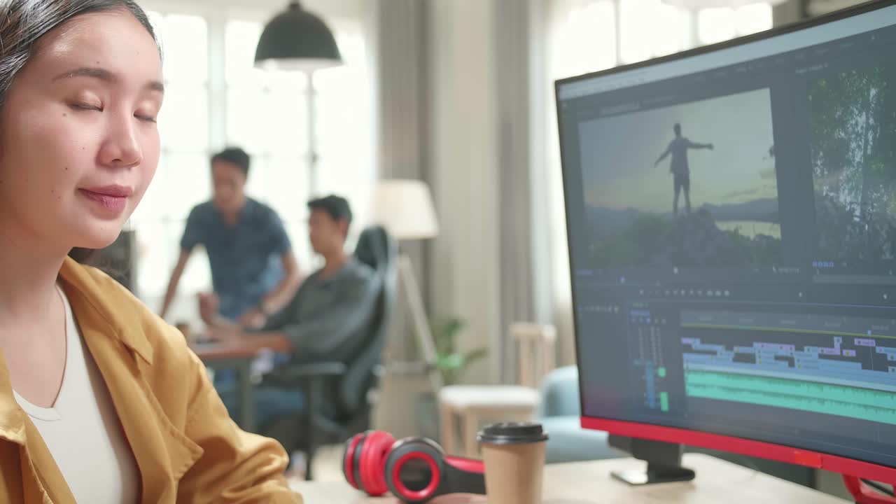 Asian Female Video Editor Works With Footage And Sound On Her Personal Computer. He Turns And Warmly Smiles Into The Camera