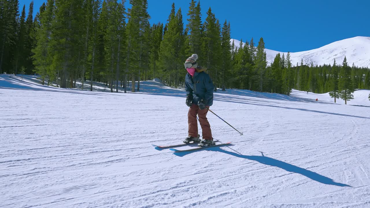 멀리 큰 산과 함께 토끼 언덕을 내려 스키를 타고 있는 여성 다운힐 스키 선수를 둘러싸고