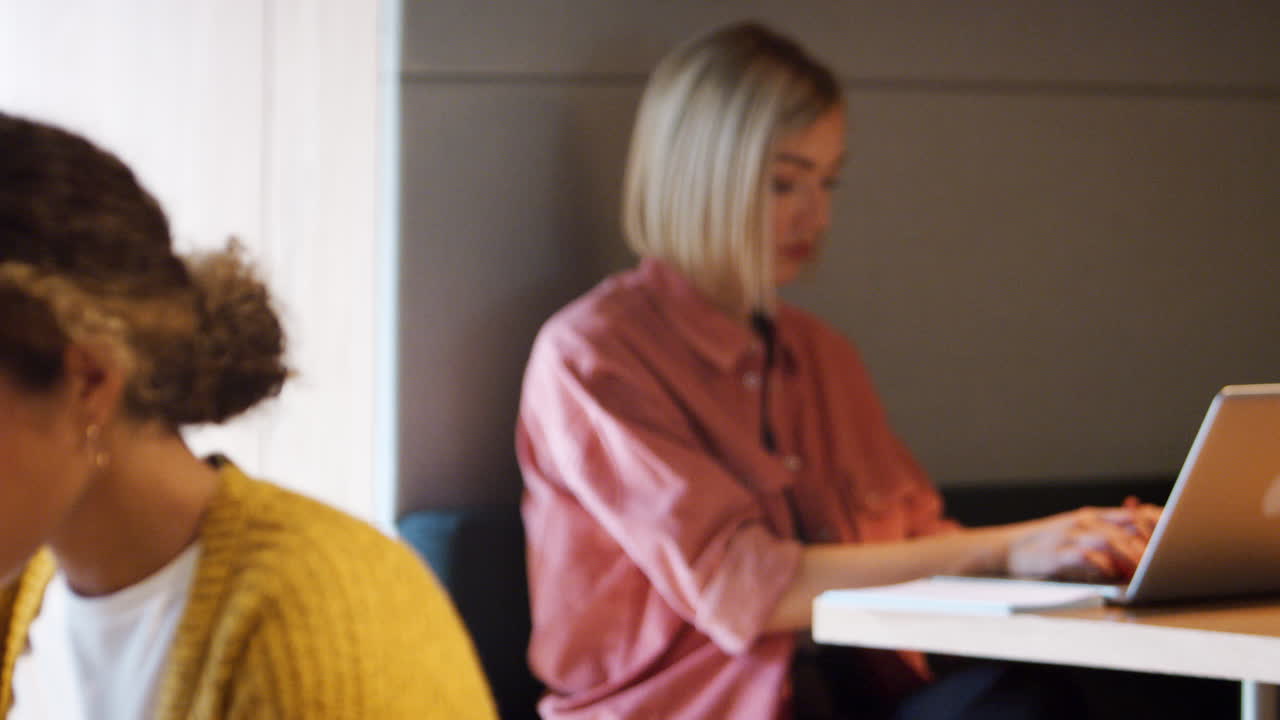 Due giovani creativi millennial lavorano al computer seduti in un ufficio, con messa a fuoco selettiva dal primo piano allo sfondo.