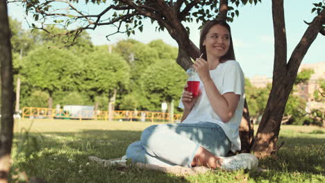woman drinking soda sitting by tree