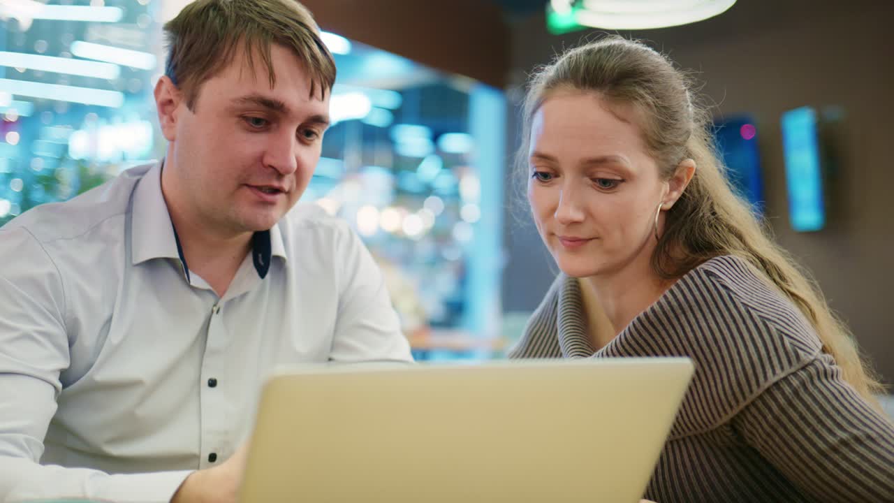Man and Woman Discussing Content on Laptop in Cafe