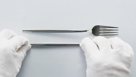 Minimalist table setting with white plate, fork, and knife arranged neatly, and a gloved hand adjusting cutlery.
