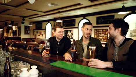 male colleagues are having conversation in local bar. coworkers meeting outside workplace and communicating informally. nice pub interior in background.