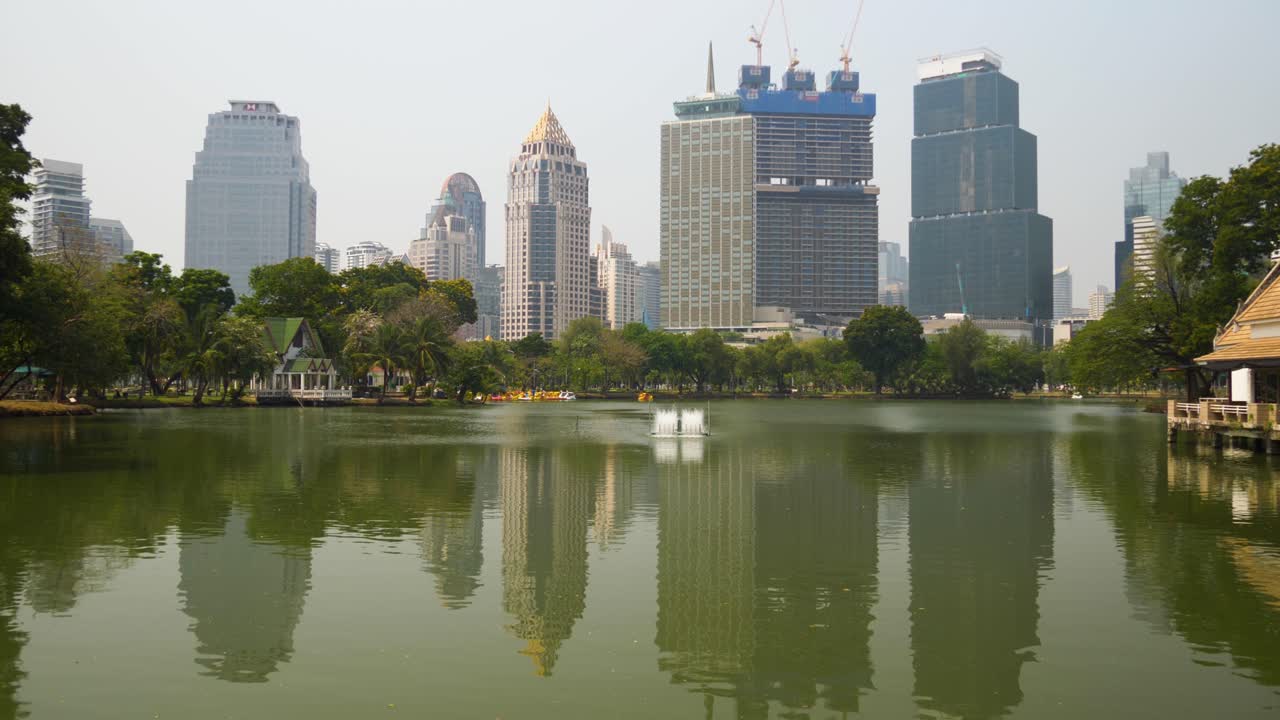 View of tall buildings in Bangkok from Lumpini Park, reflecting in a peaceful lake