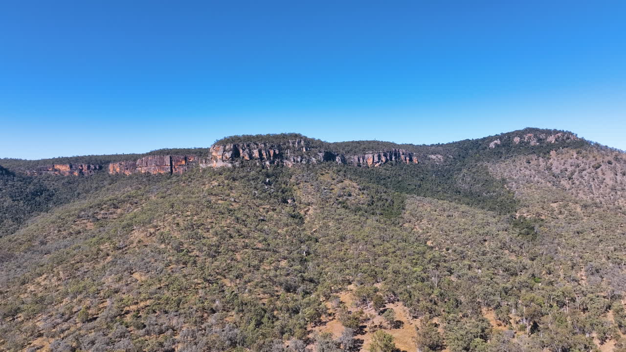 Flight rises over the sparse evergreen forests and rugged bluffs of Cania Gorge National Park and the buttresses of Castle Mountain Monto Burnett Queensland Australia