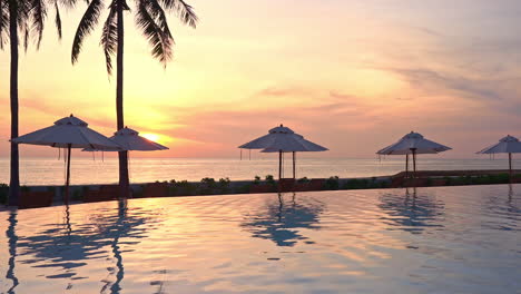 a colorful sunset on the ocean horizon reflects on a resort swimming pool and beach