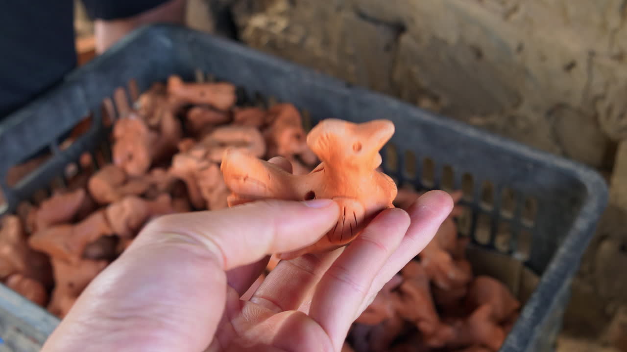 동남아시아 도자기 스타일의 수탉의 전통적인 점토 조각상을 손에 들고 있는 모습을 가까이서 볼 수 있습니다.