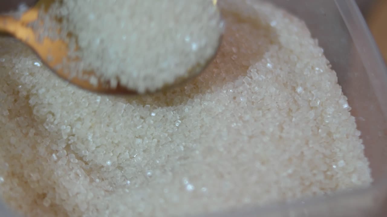 Primer plano de una cuchara removiendo azúcar granulada