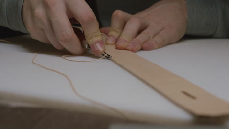 A craftsman cuts off excess leather from the brim of a raw leather belt. Focus shifting with his hands.