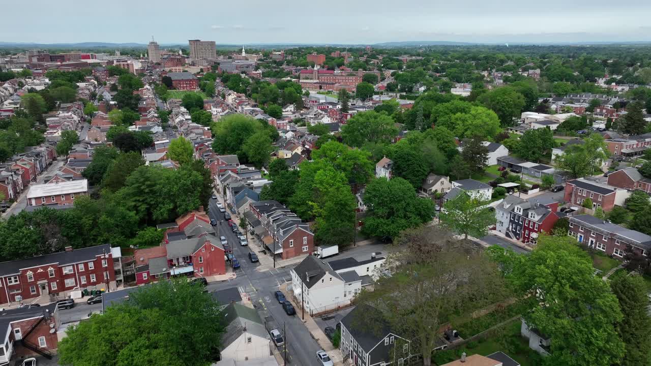 Aerial view of Lancaster, PA in spring. Lush trees line charming residential streets, historic brick homes, and blooming greenery create a peaceful small-town American atmosphere. Downtown in distance