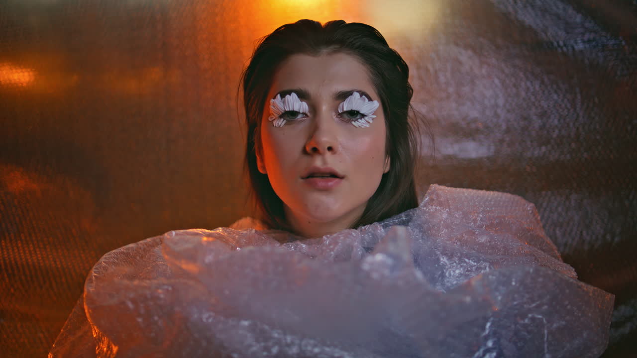 Wrapped bubble wrap woman showcasing floral eyelash art closeup. Mysterious gaze