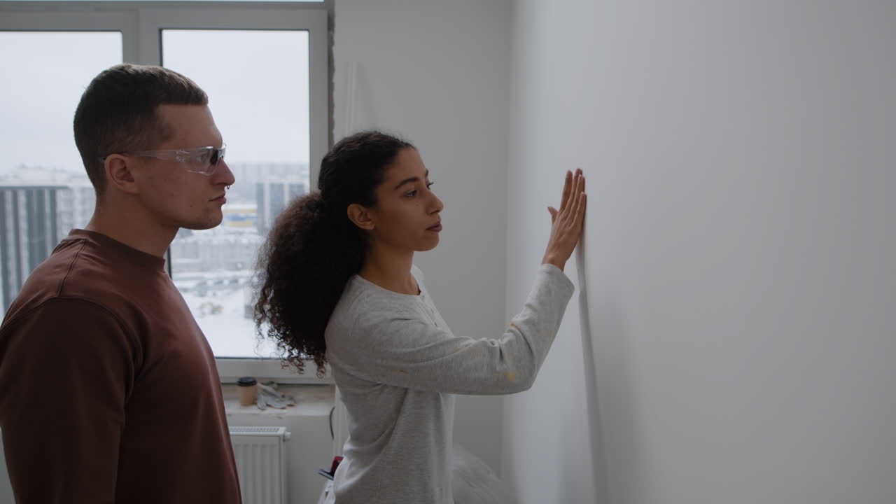 Young Couple Doing Home Improvement: Sanding and Inspecting Walls