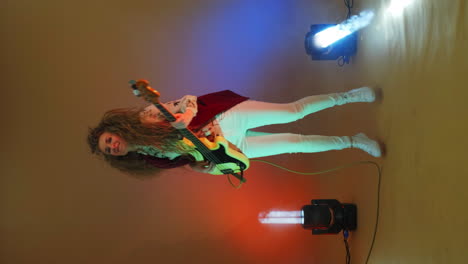 vertical video of a female bass player in a jacket jumping on one leg dancing and shaking her head and hair. crazy guitar player in the studio neon lights and spotlights