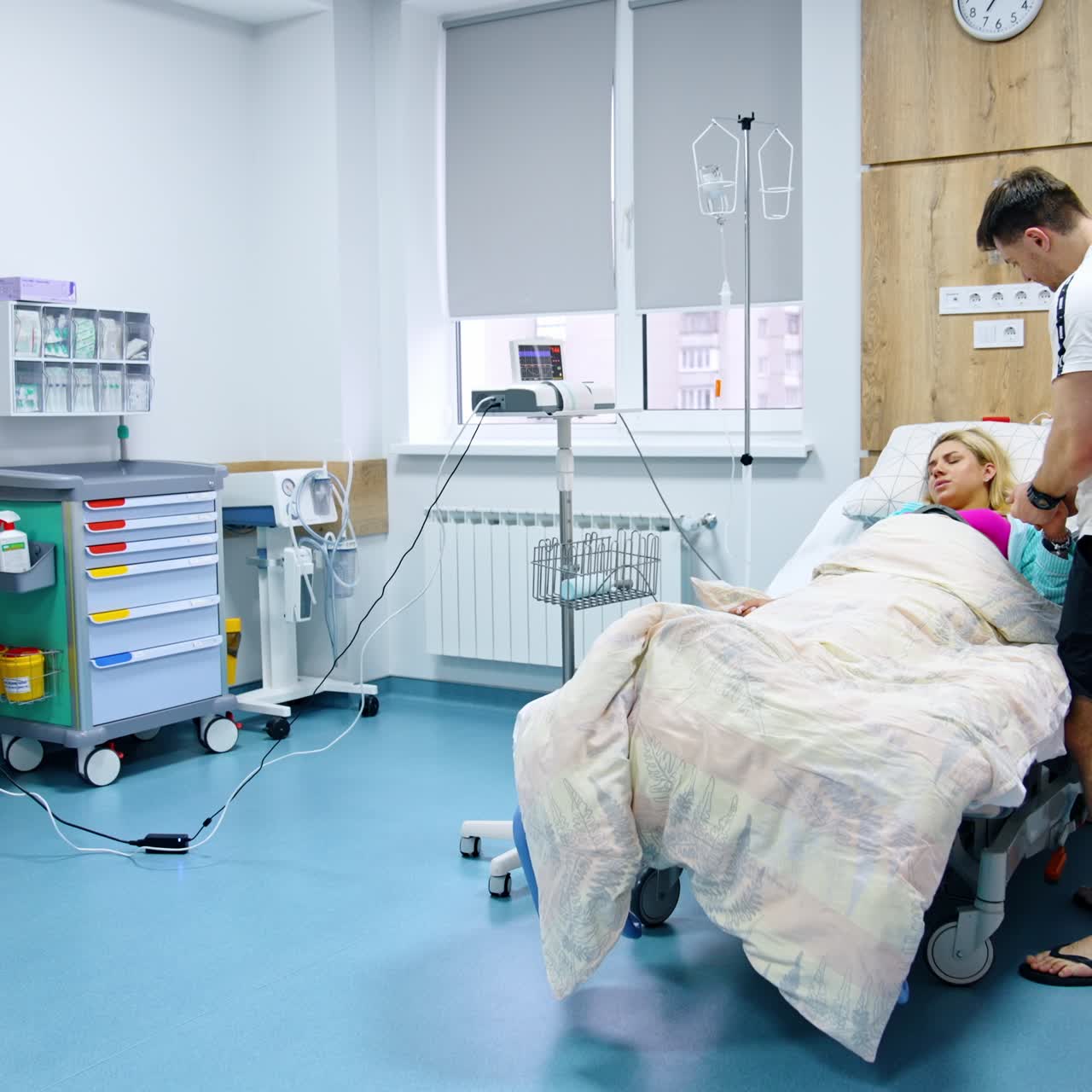 Woman feeling painful contractions lies in the hospital bed. Man standing beside comforts her stroking her head