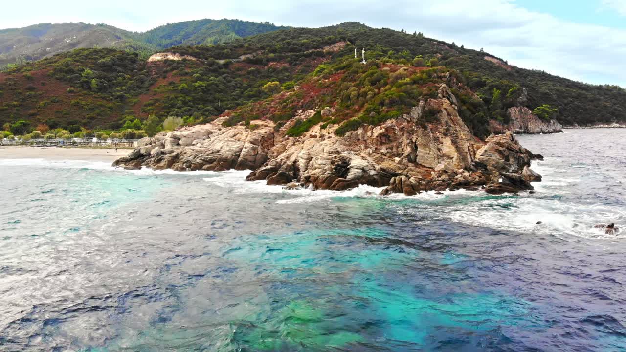 Aerial drone view of the Aegean sea coast with camping near the beach, multiple greenery, hills on the background, blue water with waves. Greece