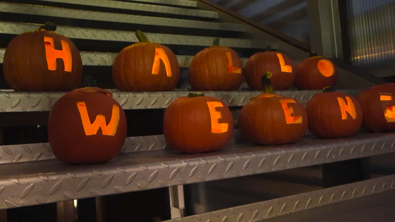 Halloween carved out pumpkins or Jack o lanterns that have candle light in them placed on metal stairs in an artistic way during night time. Glowing light makes the pumpkins spooky. Holiday time.
