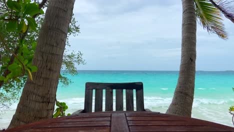 Static-shot-of-wooden-table-without-people-in-front-of-turquoise-sea-water-in-tropical-beach-of-Maldives