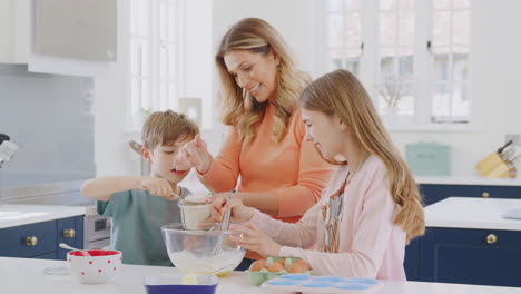 mother with two children in kitchen at home having fun baking cakes together