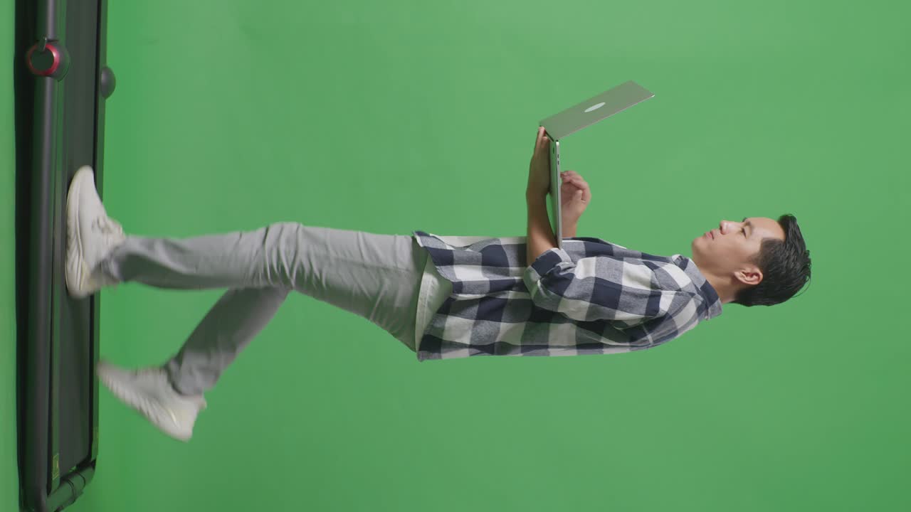 vista lateral del cuerpo completo de un hombre asiático usando una computadora portátil mientras camina en el estudio de pantalla verde