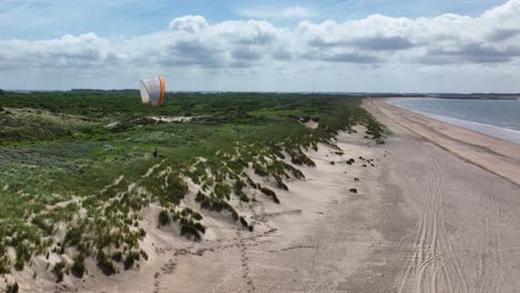 lone paraglider drifting along lush seaside sand dune vegetation on dutch beacheuro