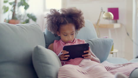 cute black girl enjoying mobile game on tablet lying in bed