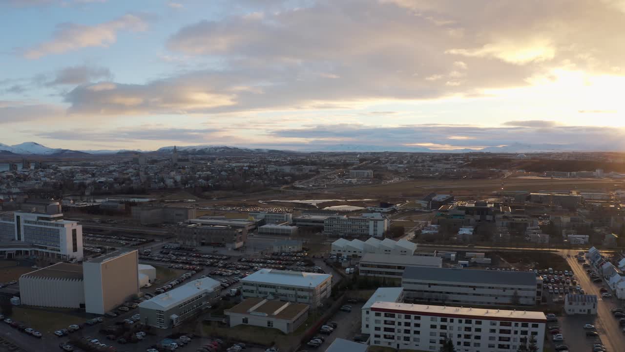 Drone Flying over the snowy Rooftops of the Reykjavik, Iceland During a Fantastic Sunset that Flares over Mountain Tops towering over city
