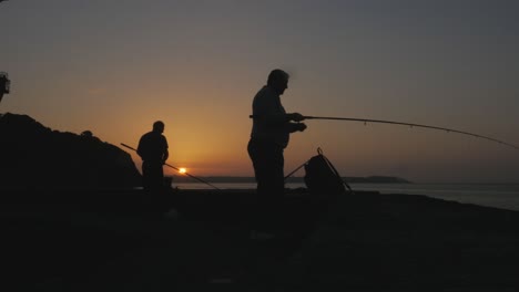 Wunderschöne-Silhouette-Von-Fischern,-Die-Bei-Sonnenaufgang-Ihre-Angelruten-Auswerfen,-Frühaufsteher-Fangen-Den-Wurm