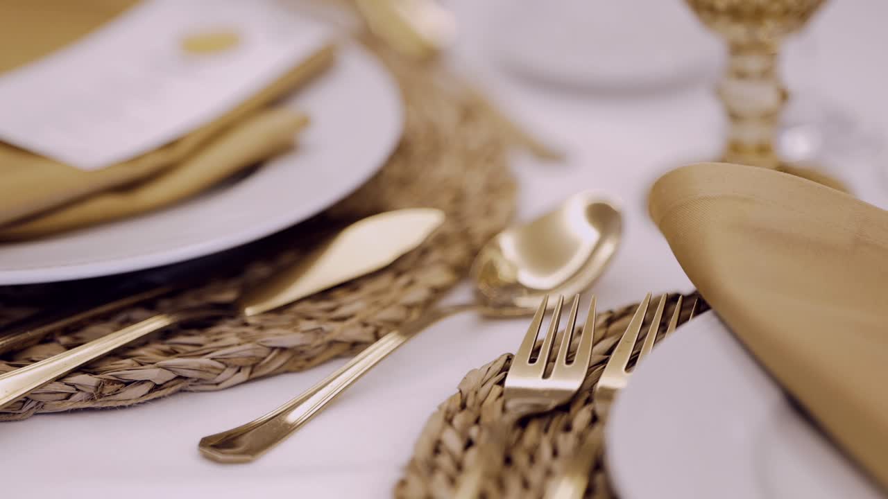 Close up of gold cutlery on a woven placemat with elegant napkins and plates