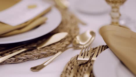 close up of gold cutlery on a woven placemat with elegant napkins and plates