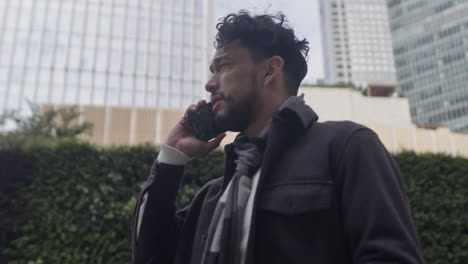 pivot around a middle aged man of hispanic ethnicity standing in downtown business district and talk seriously on the phone