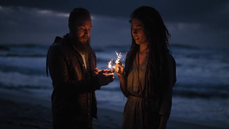 una pareja joven en la playa encendiendo bengalas celebrando la víspera de año nuevo disfrutando de una velada divertida juntos en un tranquilo fondo marino junto al mar por la noche