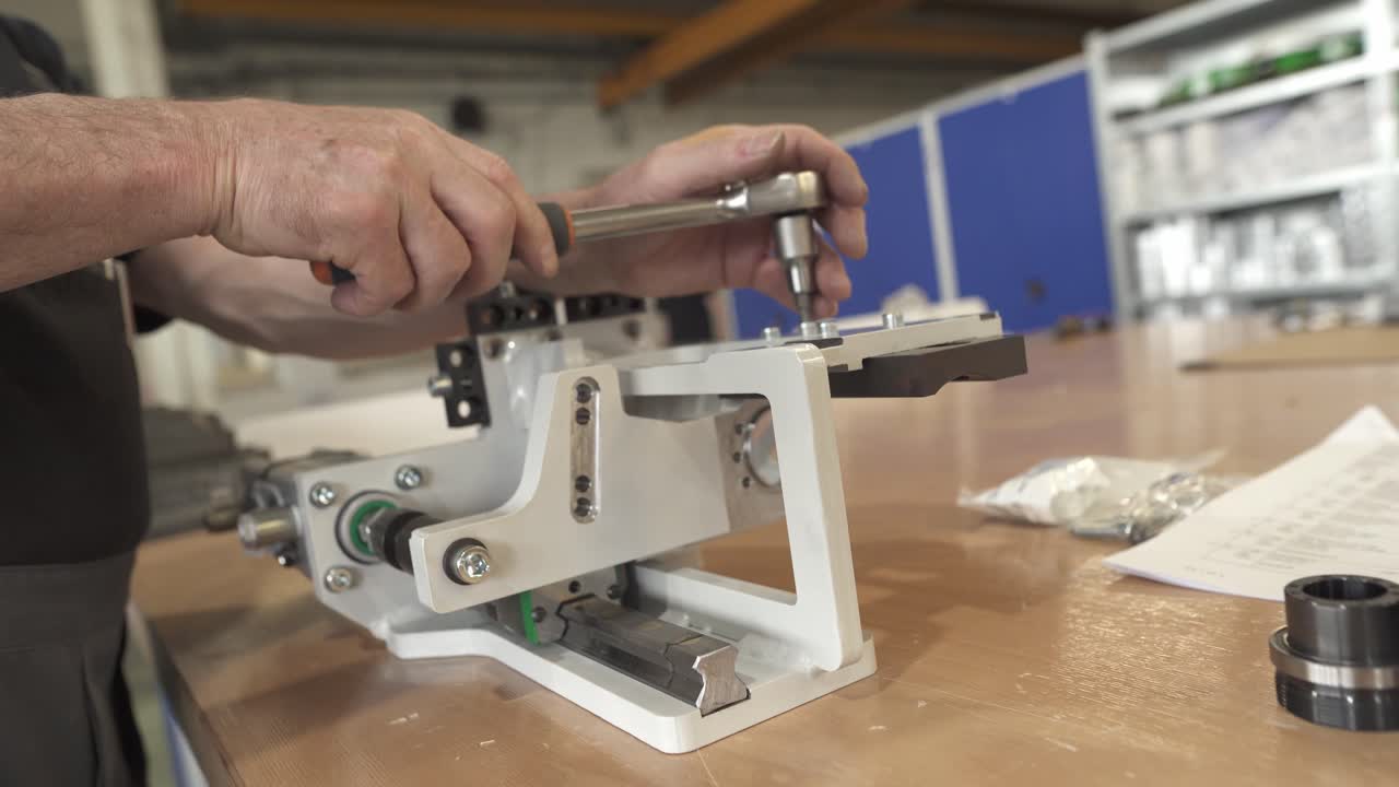 Technician tightens a bolt on a precision linear guide mechanism. Close up of mechanical positioning unit assembly in a workshop environment