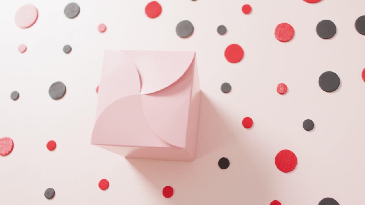 Overhead view of pink gift box on white background with red and black dots